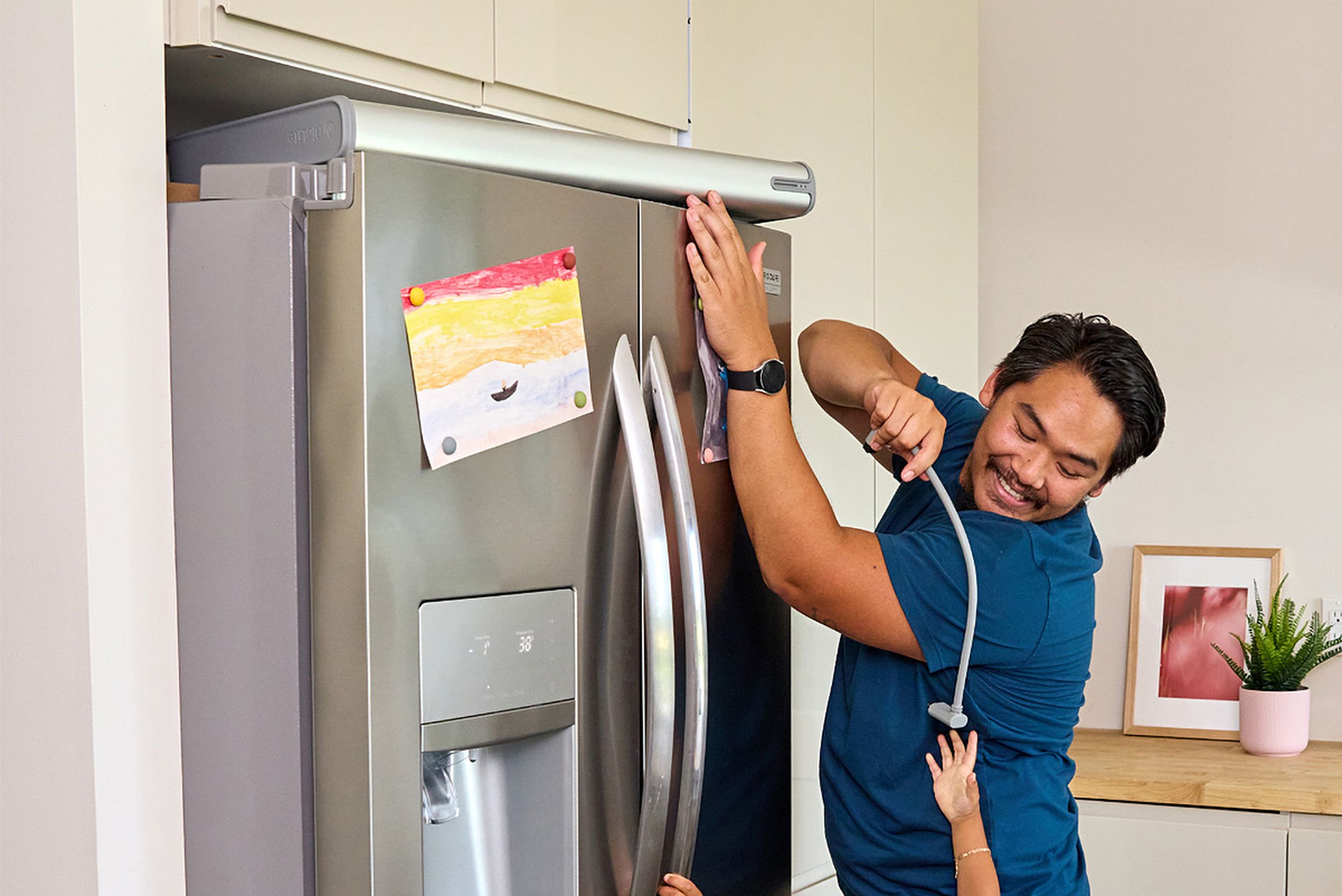 A person is placing a Backup by BioLite battery on top of a refrigerator, while a child reaches for a dangling power cord.