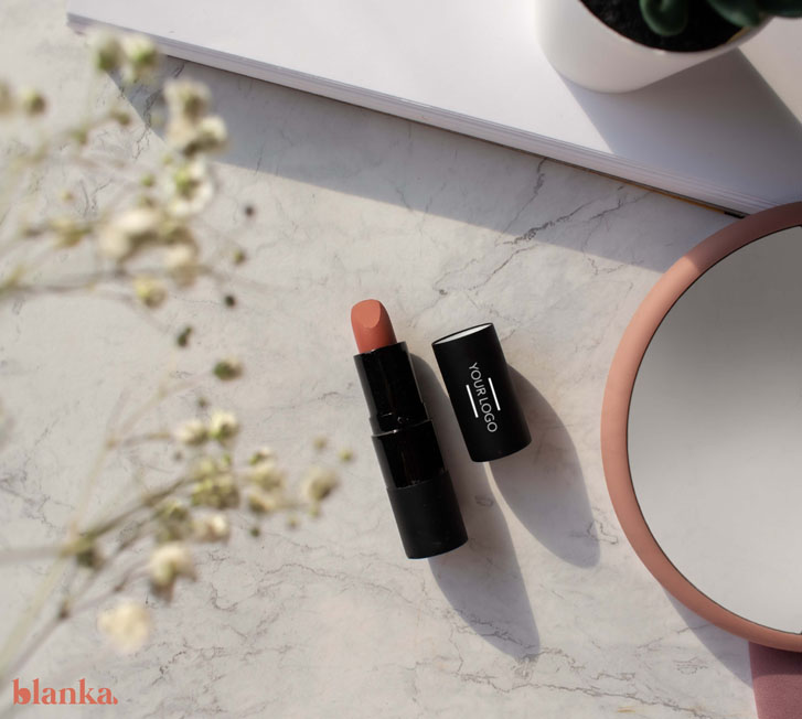 an open lipstick on a marble surface with a mirror beside it